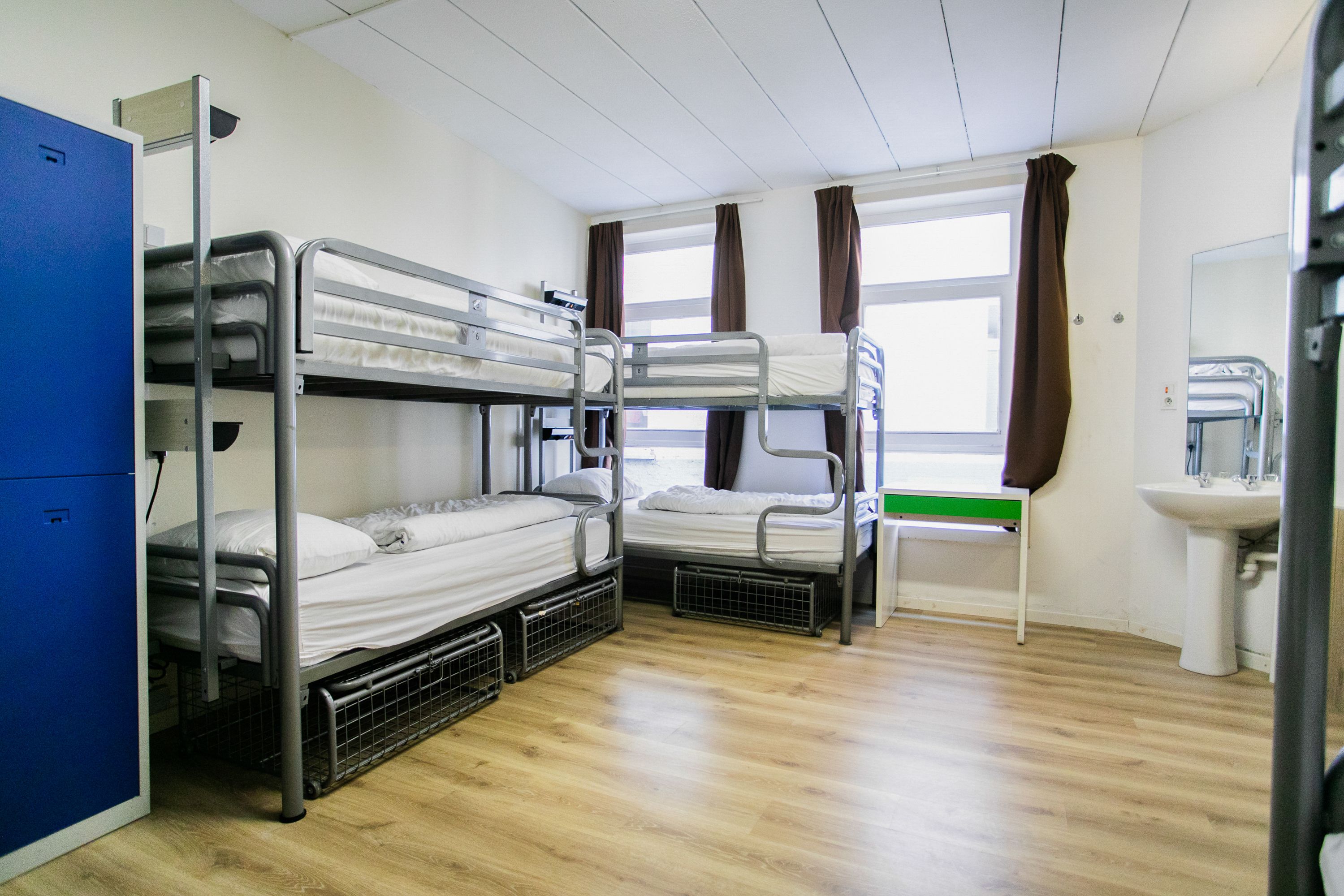 Een slaapzaal met twee stapelbedden, een wastafel en een raam met gordijnen.