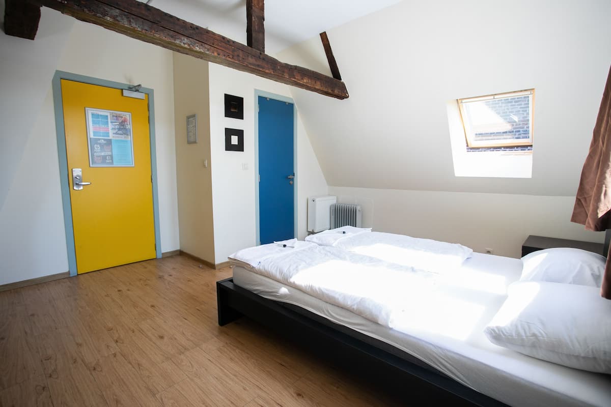 Een slaapkamer met een houten vloer, een bed met wit beddengoed, een blauwe deur en een raam met uitzicht op de lucht.