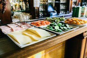 Een buffet met diverse etenswaren, zoals plakjes ham, kaas, komkommers en sinaasappels.