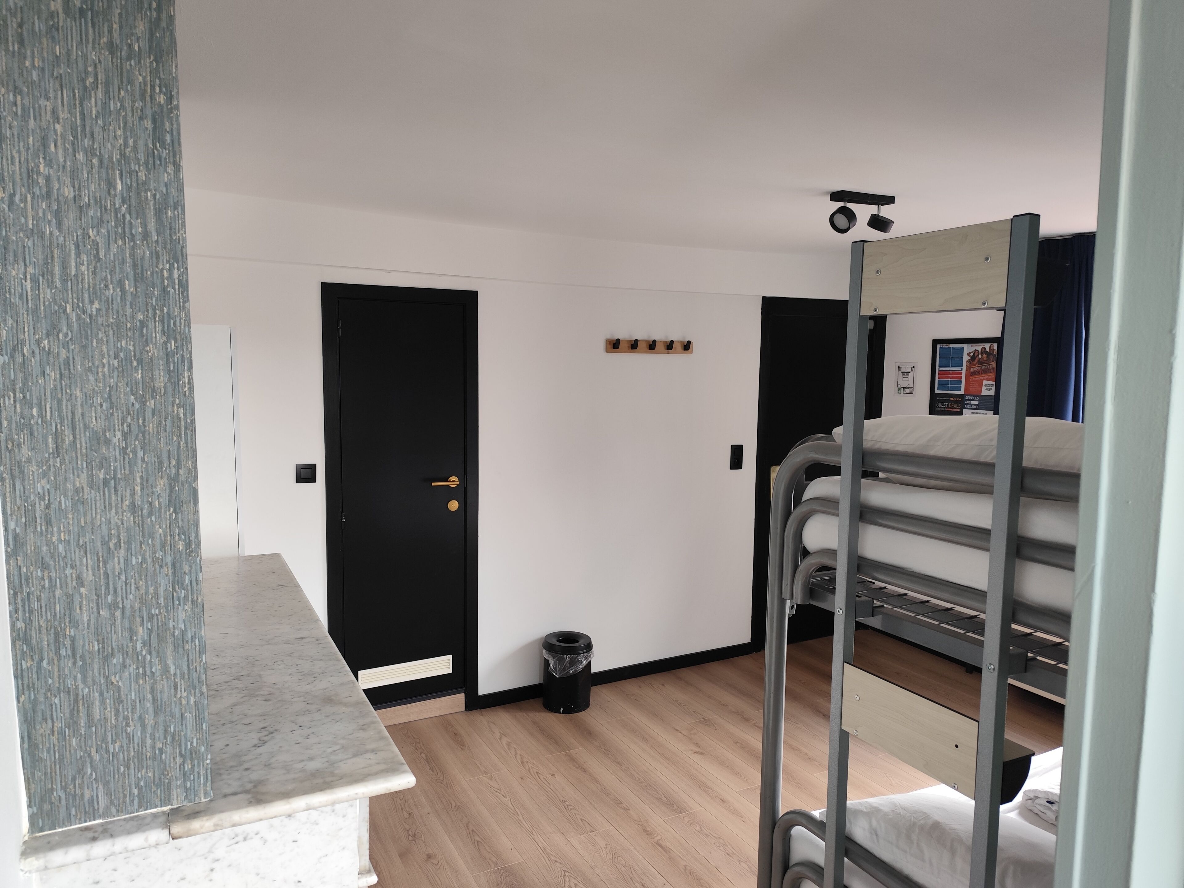 A compact room with a bunk bed, a small trash bin, a door, and a light switch on the wall.