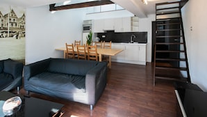 Una sala de estar moderna con sofá, una mesa de comedor con sillas, una zona de cocina y una escalera de madera.