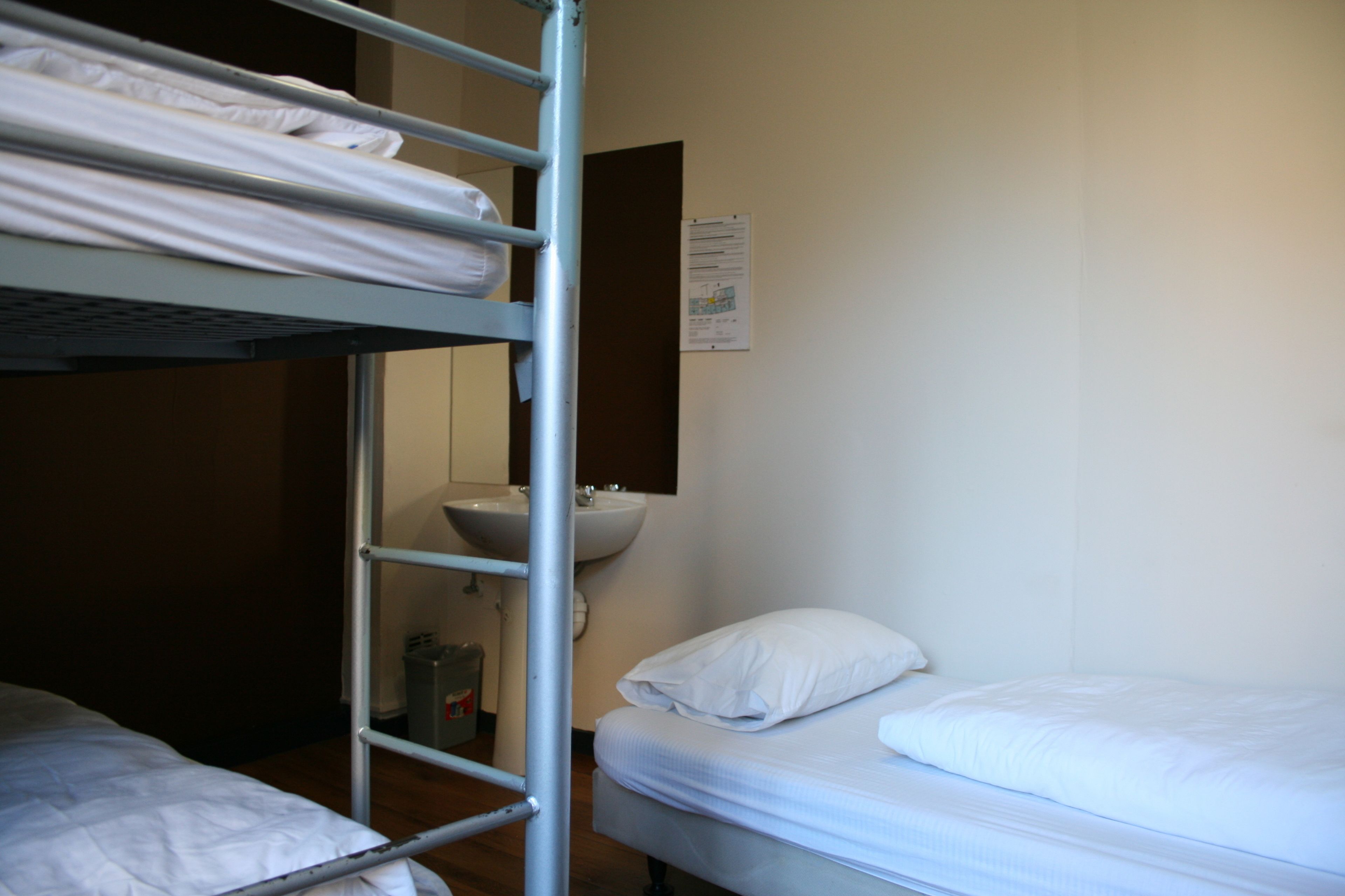 A dormitory room with bunk beds, a sink, and a mirror.