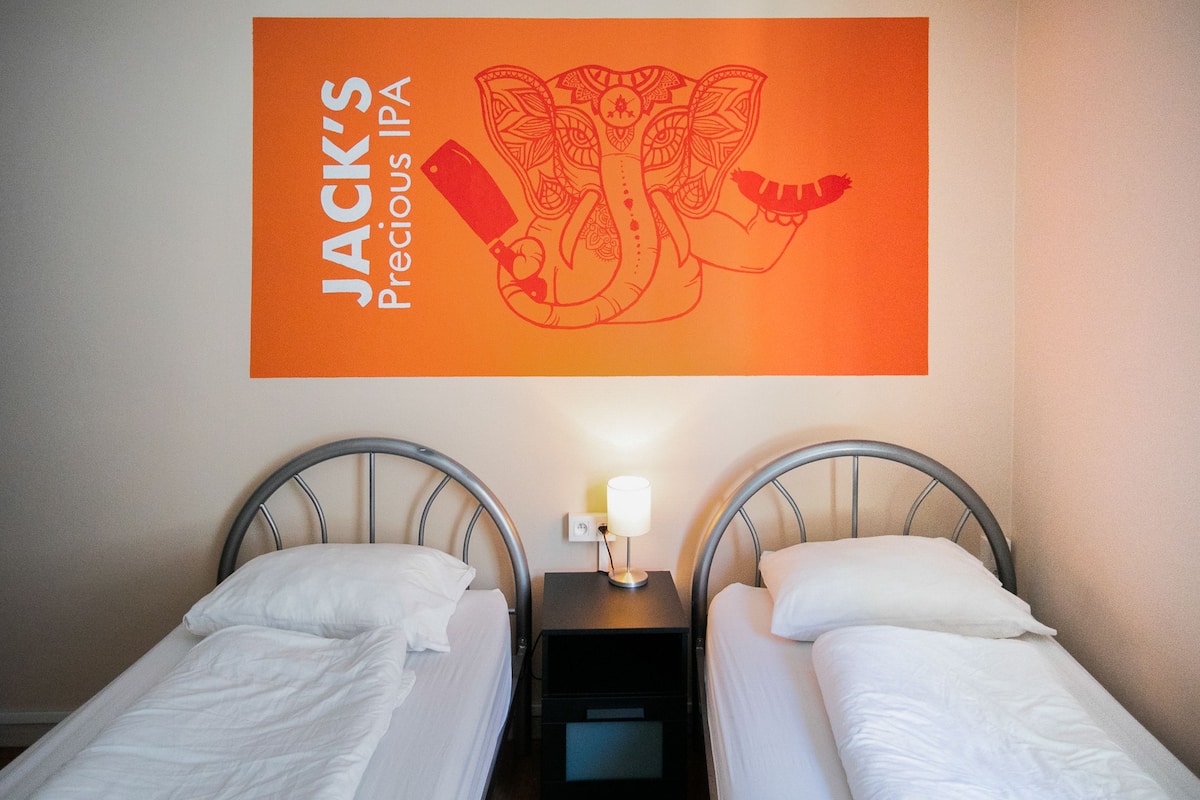 Een hotelkamer met twee enkele bedden, een nachtkastje met een lamp, en een bord aan de muur met de tekst 