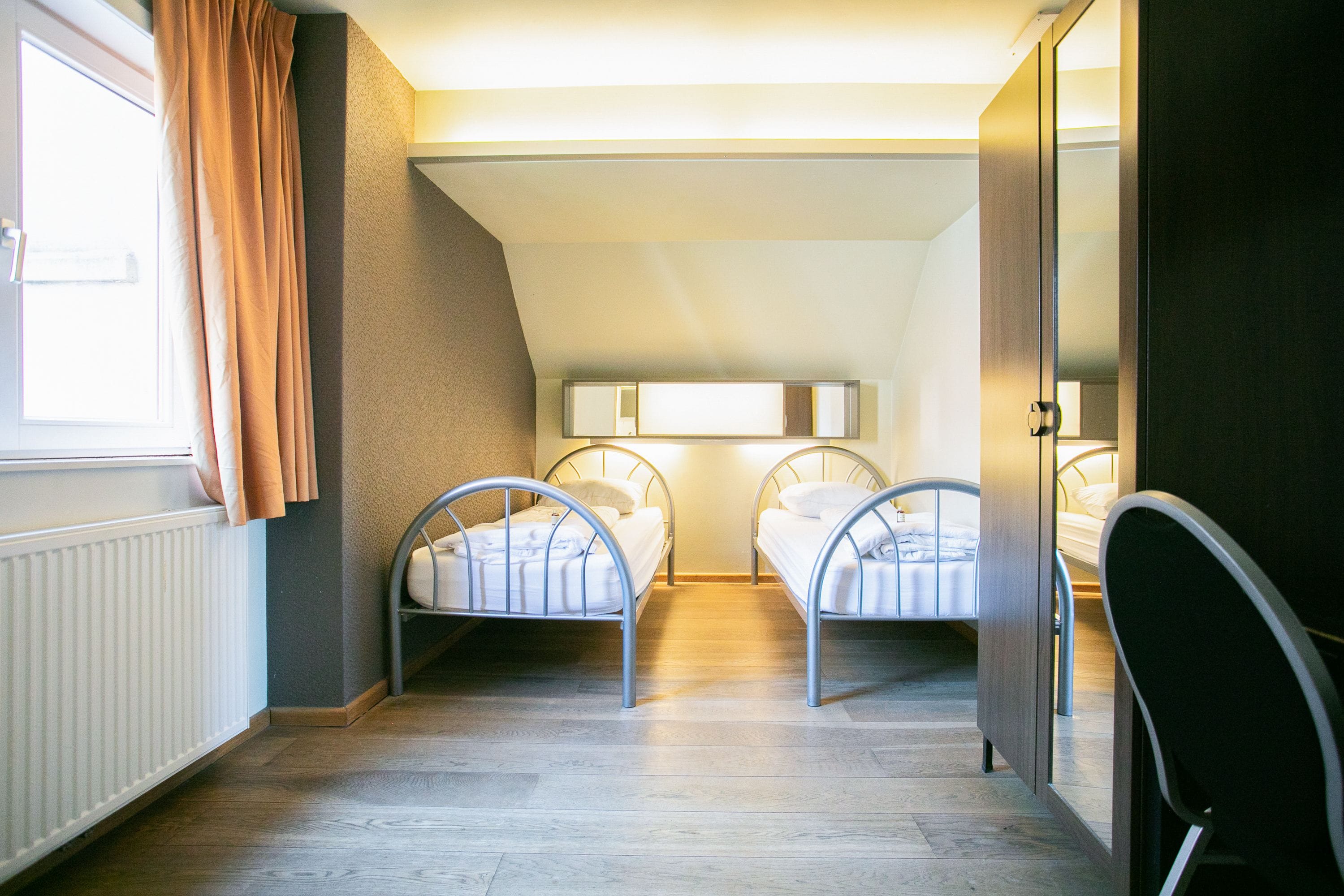 Une chambre avec deux lits superposés en métal, une fenêtre avec des rideaux et un radiateur.