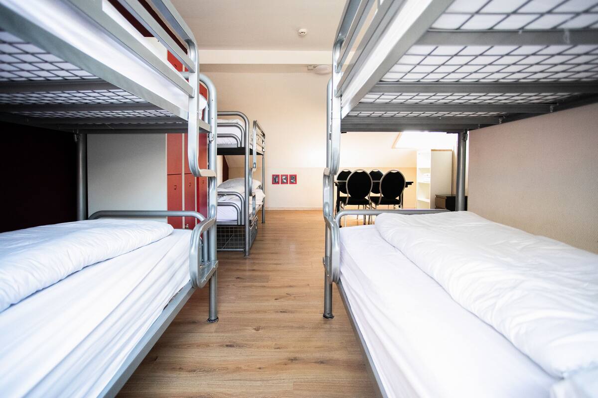 Een studentenkamer met stapelbedden, houten vloeren en een klein keukenhoekje.