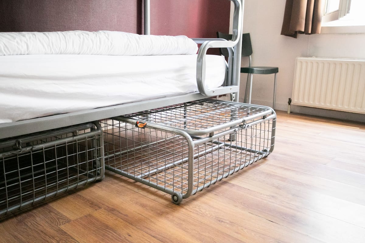 Een metalen bedframe met een matras en een metalen opbergunit eronder.