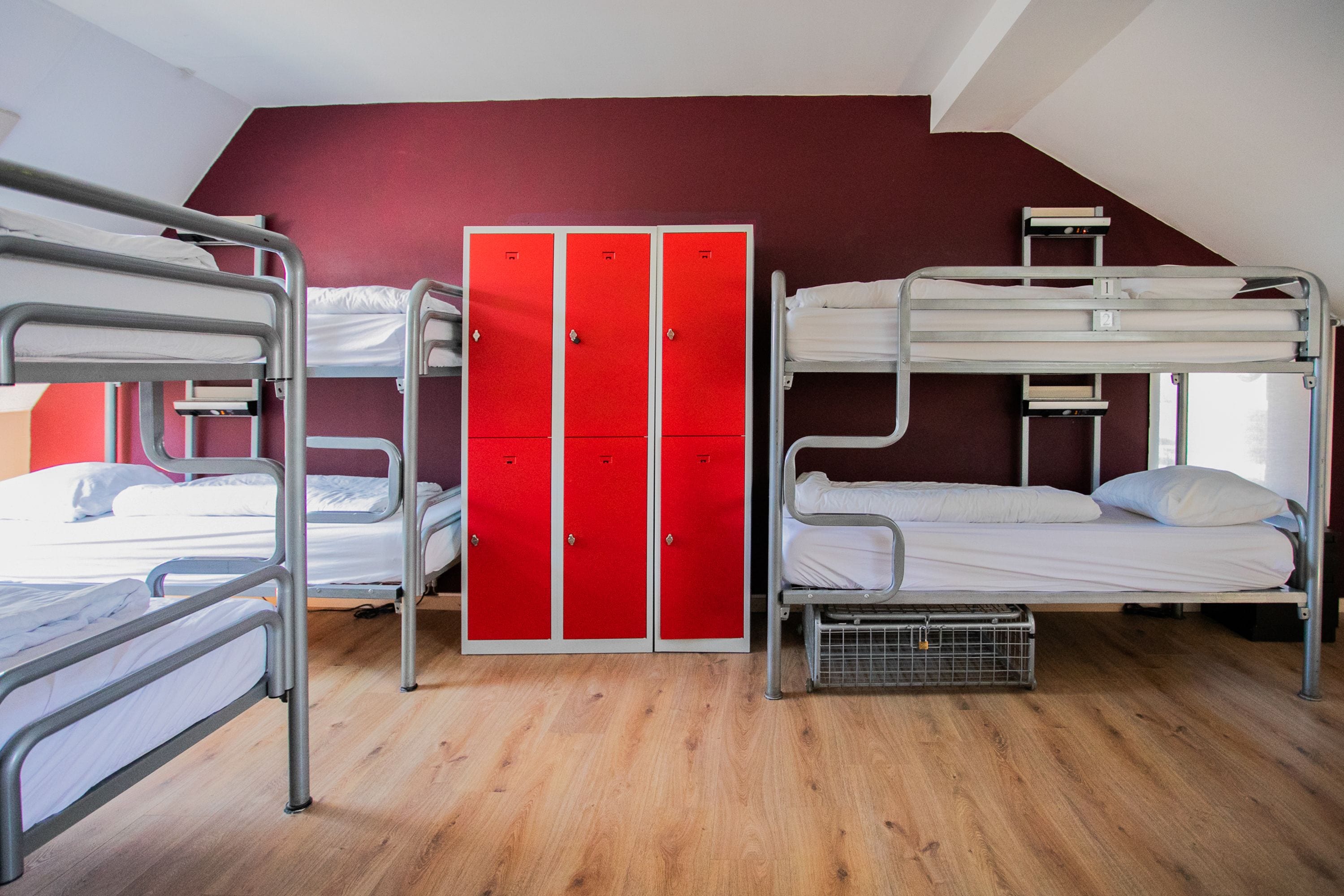 A dormitory room with bunk beds, a red wardrobe, and a wooden floor.