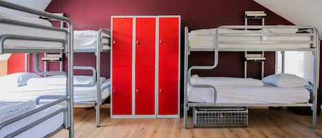 A dormitory room with bunk beds, a red wardrobe, and a wooden floor.