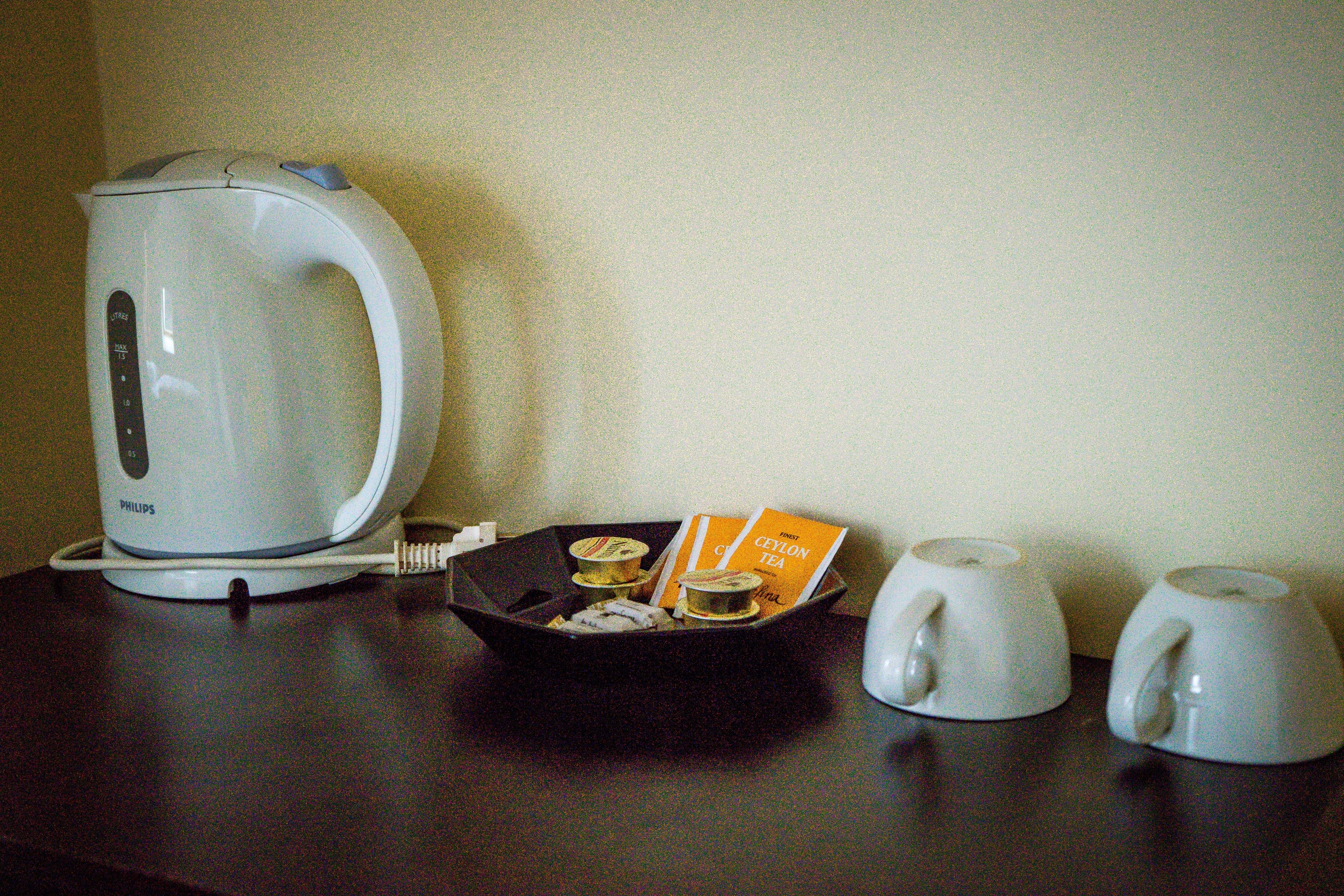 A white electric kettle, a tray with tea bags, and two white cups on a dark surface.