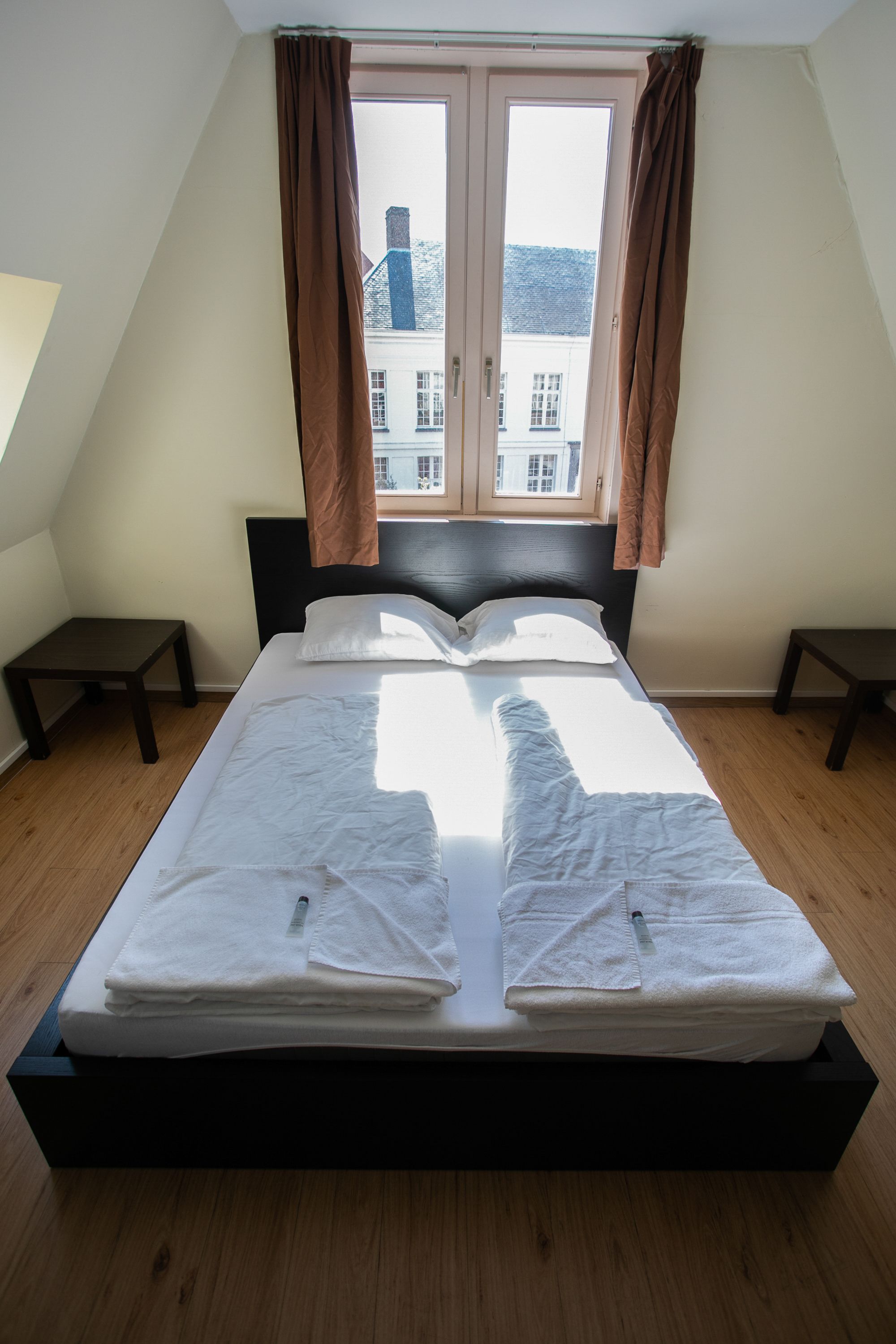 A neatly made bed with white linens and towels, a black headboard, and a window with curtains.