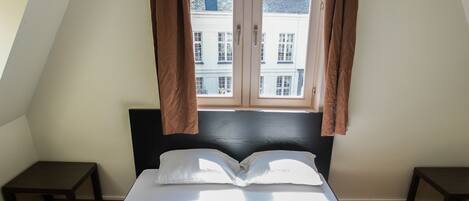 A neatly made bed with white linens and towels, a black headboard, and a window with curtains.