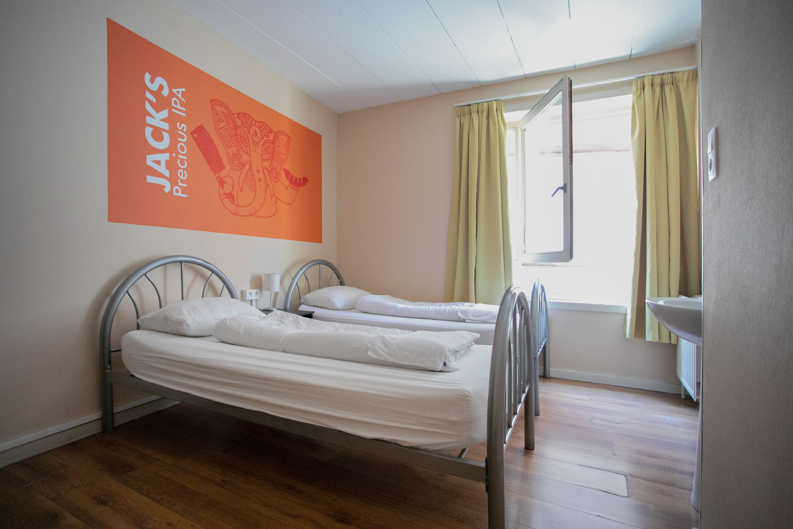Een hotelkamer met twee bedden, een raam met gordijnen en een muur met een poster.