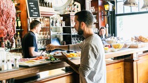 Un bar con mostradores de madera, estantes con botellas y vasos, y un menú en una pizarra.