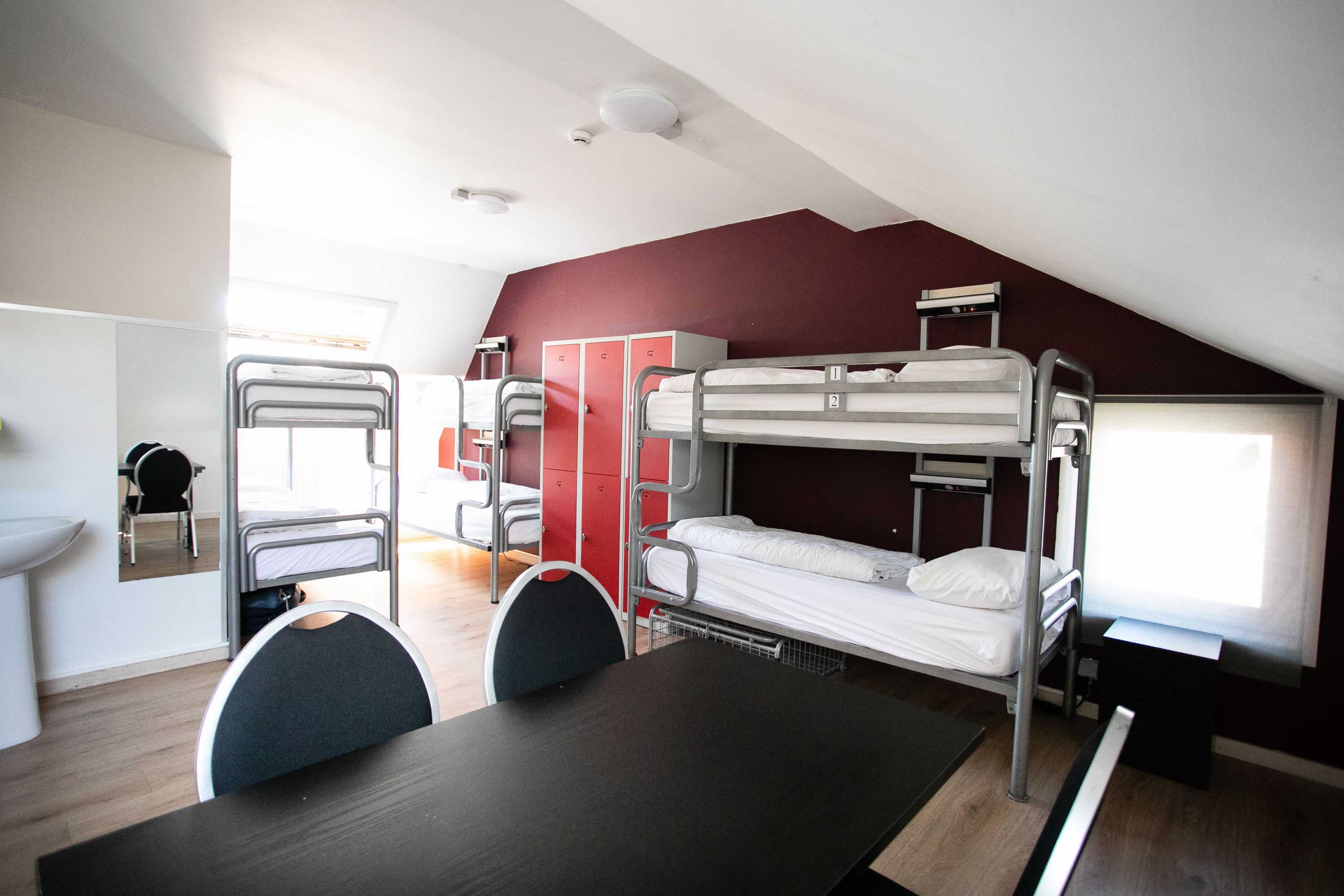 Een studentenkamer met stapelbedden, een bureau, stoelen, een spiegel en een raam.