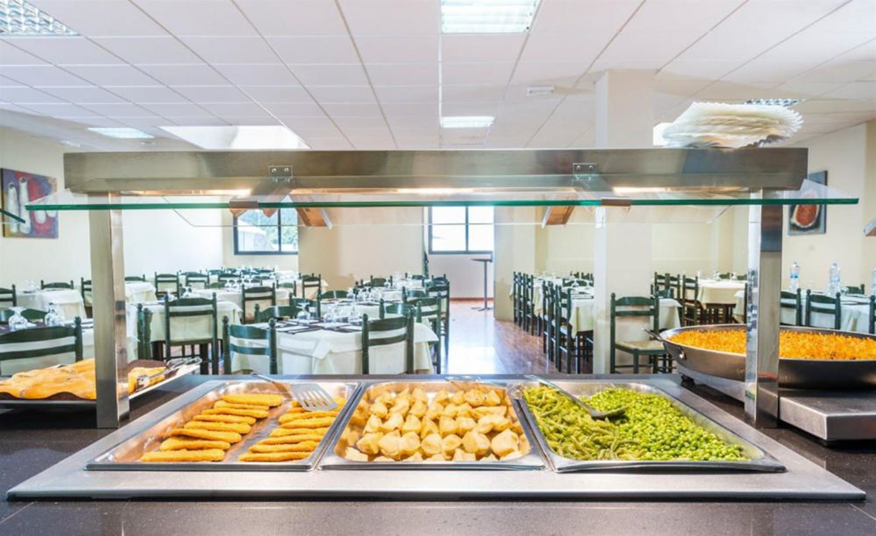 Zona de bufé con diversas opciones de comida, que incluyen frituras y ensaladas, en un amplio comedor con múltiples mesas y sillas.