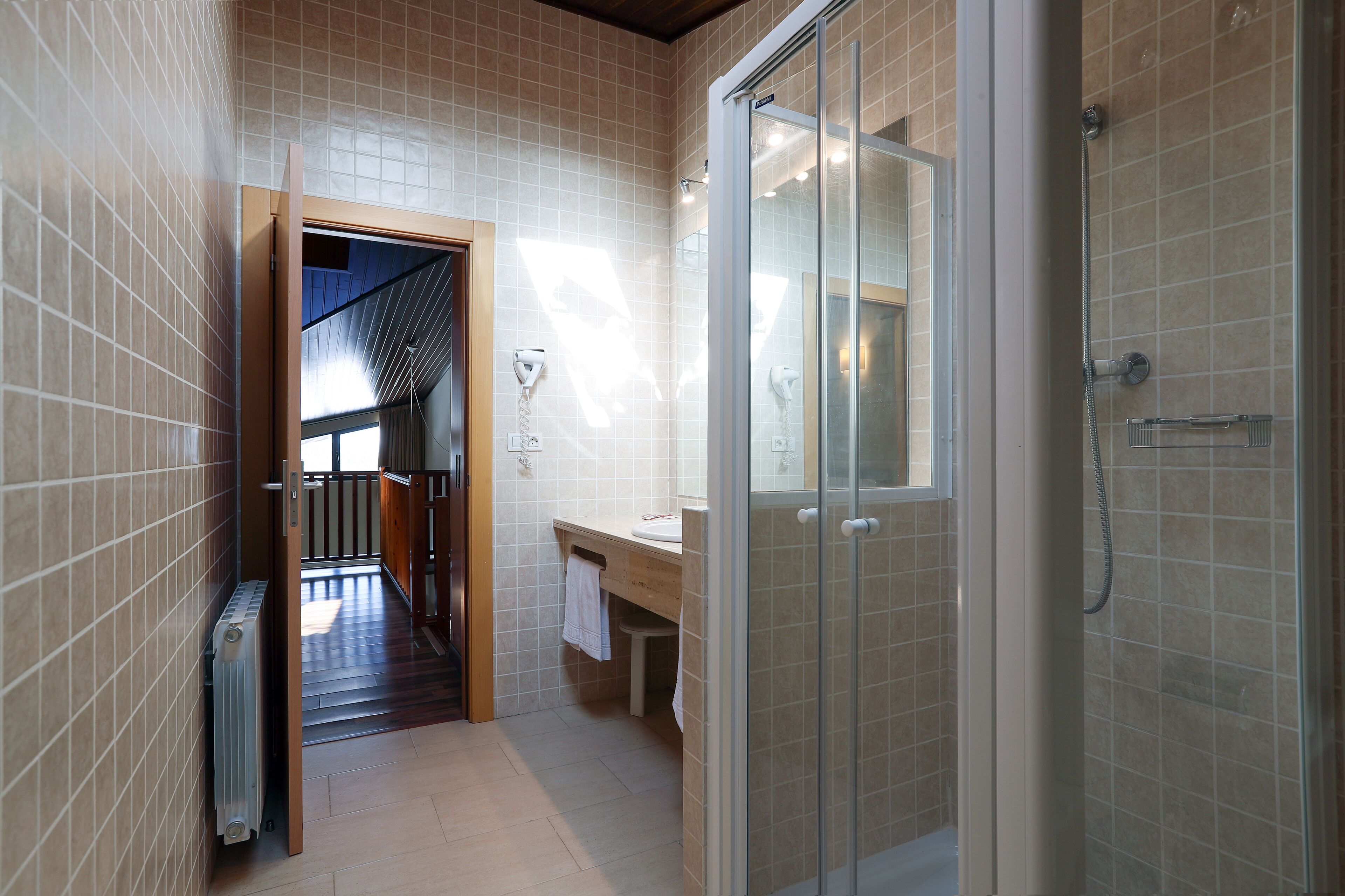 A modern bathroom with a glass shower enclosure, a wooden bench, and a visible towel rack.