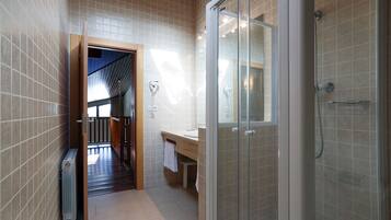 Un baño moderno con cabina de ducha de vidrio, un banco de madera y un toallero visible.