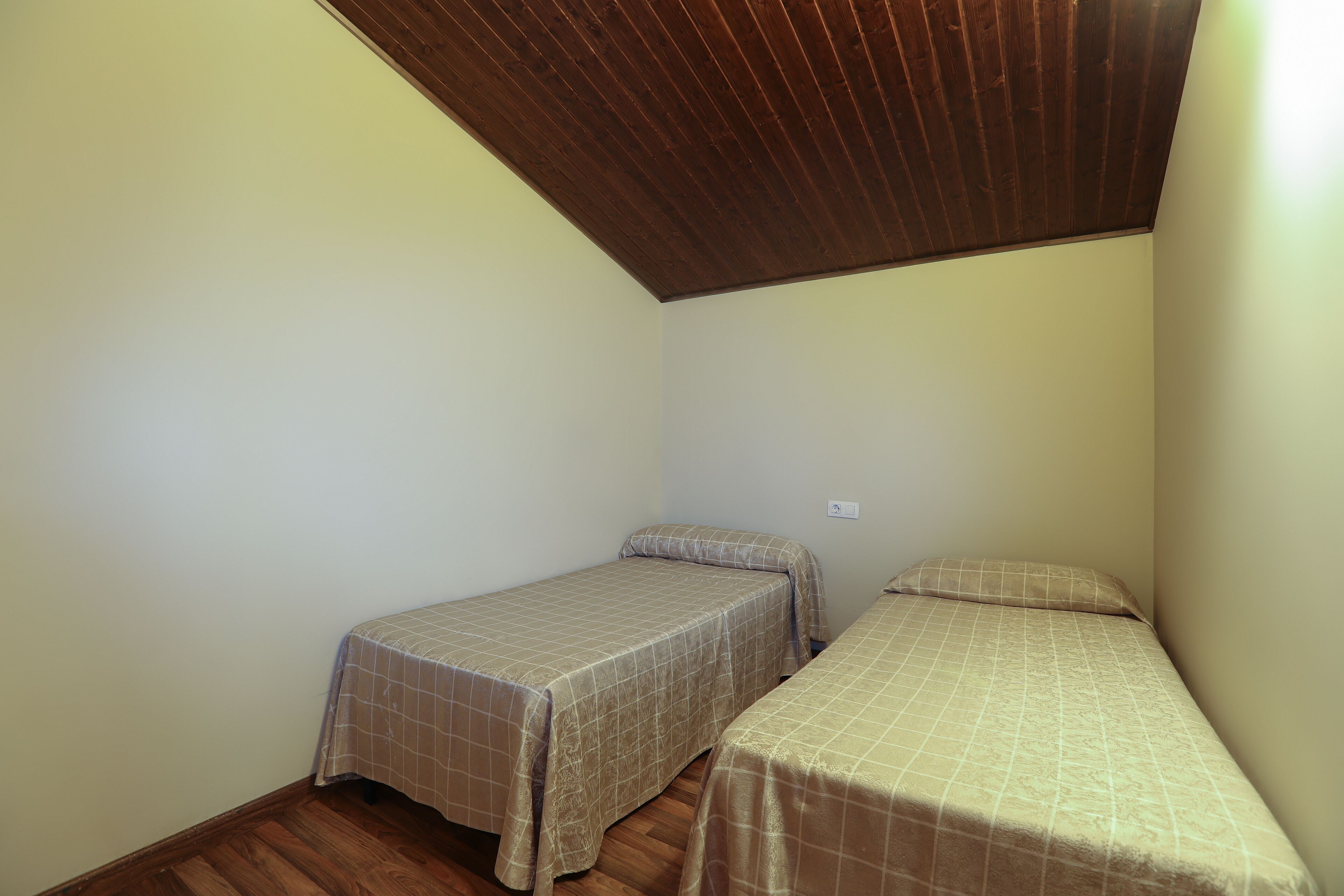 A small room with two single beds, wooden flooring, and a sloped ceiling.
