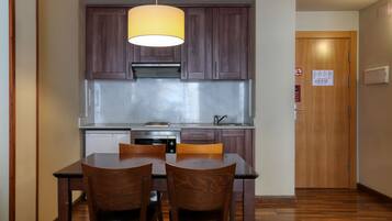 Una cocina compacta con armarios de madera oscura, un refrigerador de acero inoxidable y una mesa con sillas.