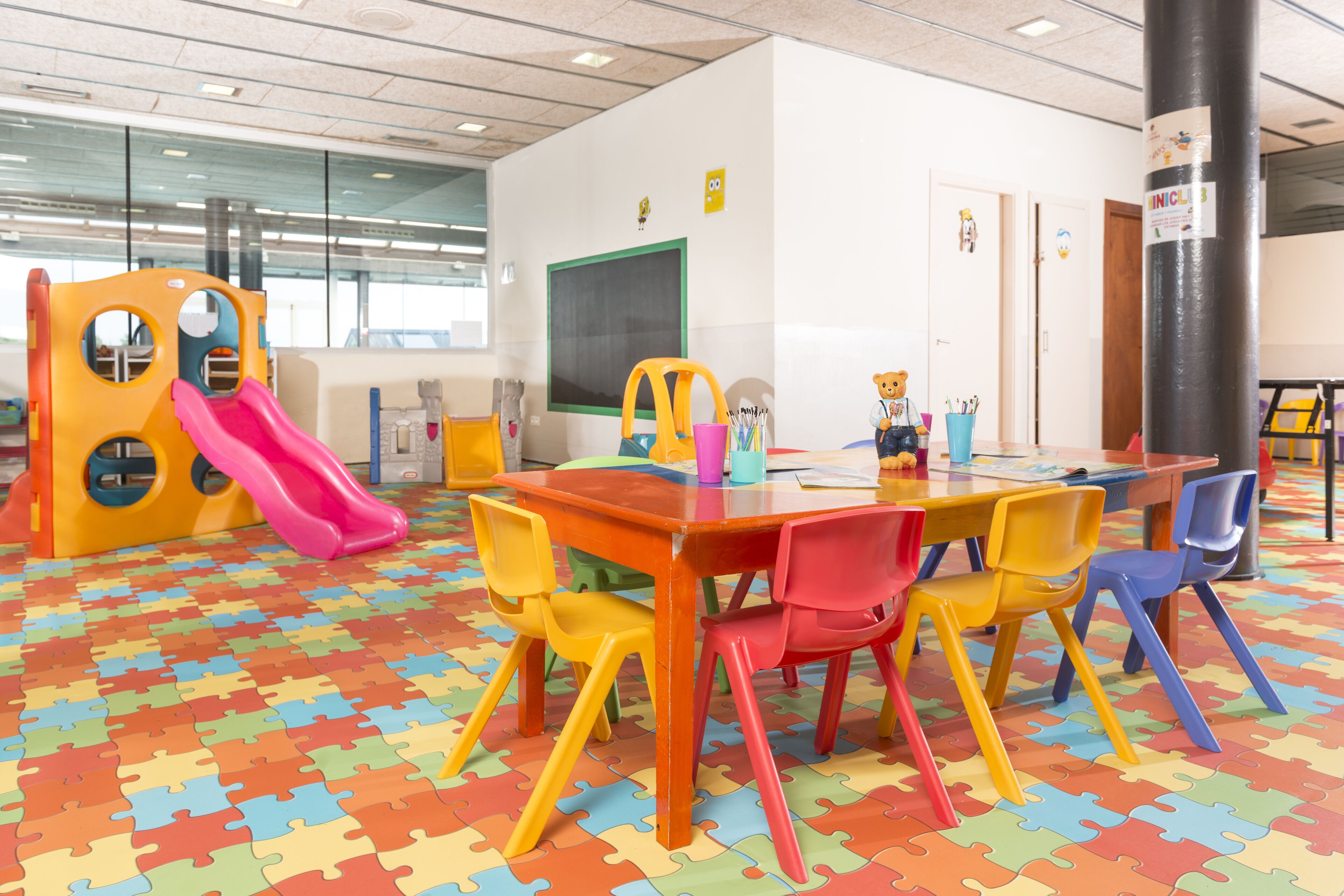 A children's play area with a slide, colorful chairs, and a table with toys.