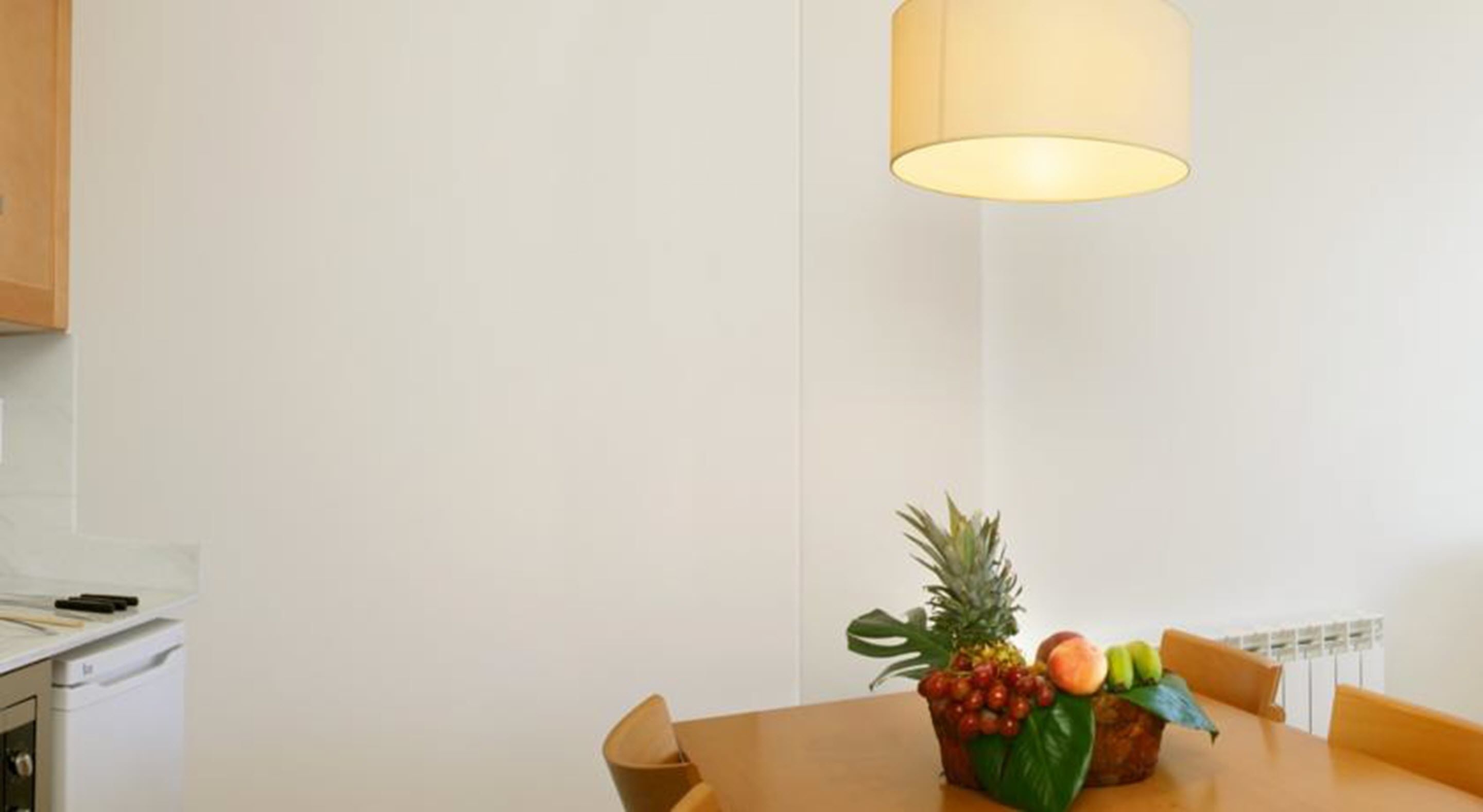 A dining area with a table set for two, a fruit bowl on the table, and a hanging light fixture above.