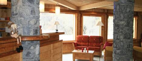 Un interior acogedor con pilares de piedra, muebles de madera y grandes ventanales.