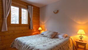 Un dormitorio acogedor con piso de madera, una cama con ropa de cama floral, dos lámparas de noche y una ventana con cortinas.