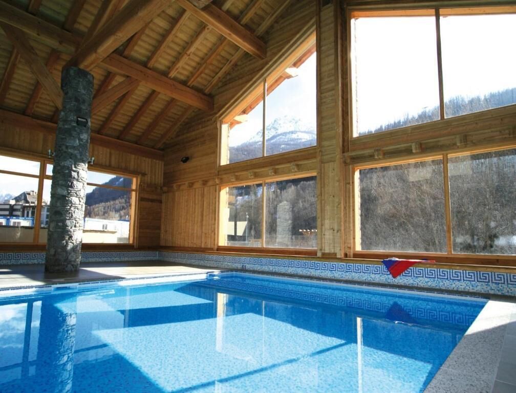 Un espace piscine agrémenté d’un pilier en pierre, de poutres en bois et de grandes fenêtres offrant une vue sur les montagnes.