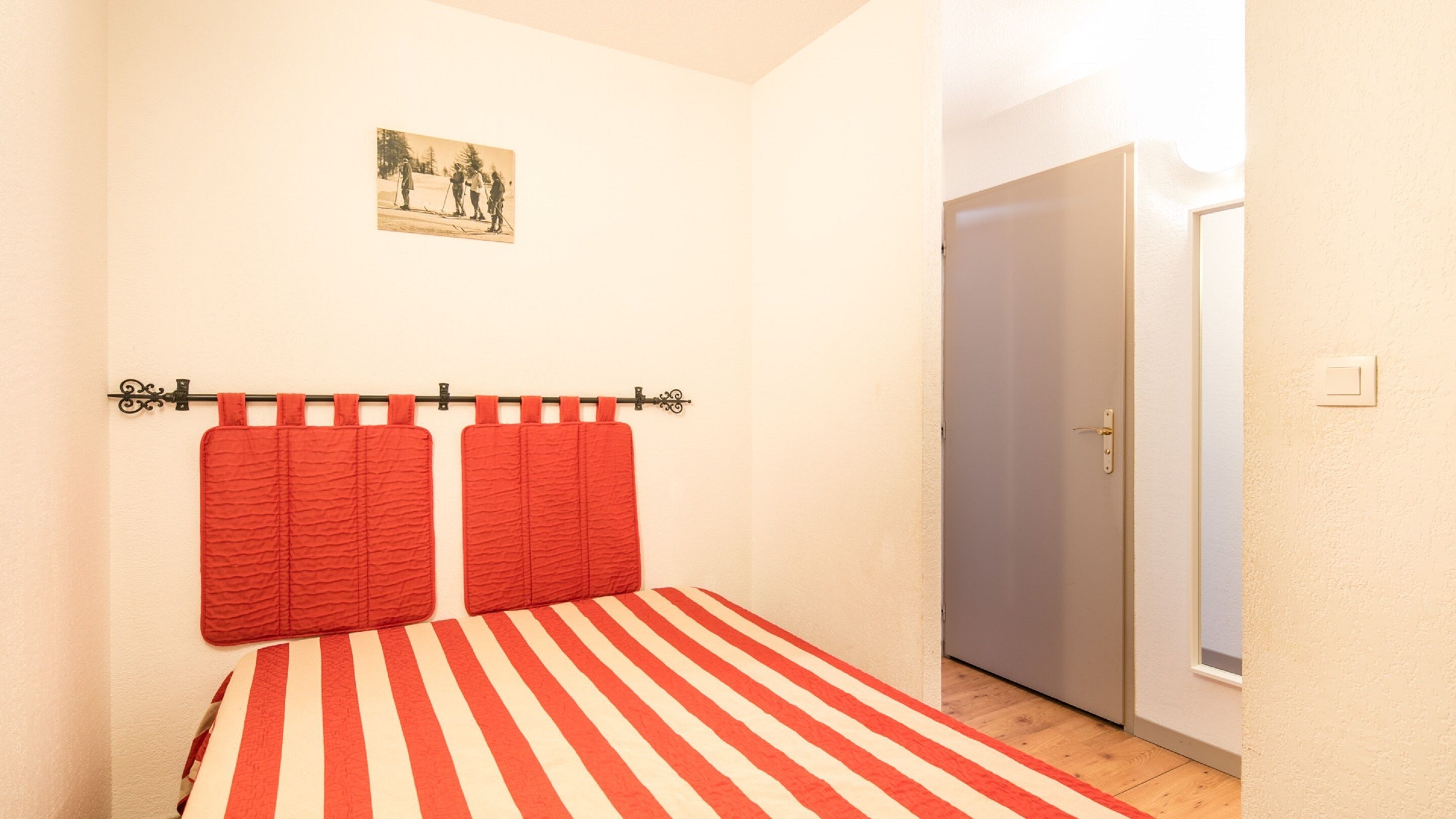 A bedroom with a striped bedspread, a red curtain, and a door to the right.