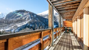 Un balcón de madera con vistas a montañas nevadas y un valle boscoso.