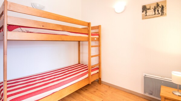 A bunk bed room with a red and white striped mattress, a wooden ladder, a wall-mounted light, and a radiator.