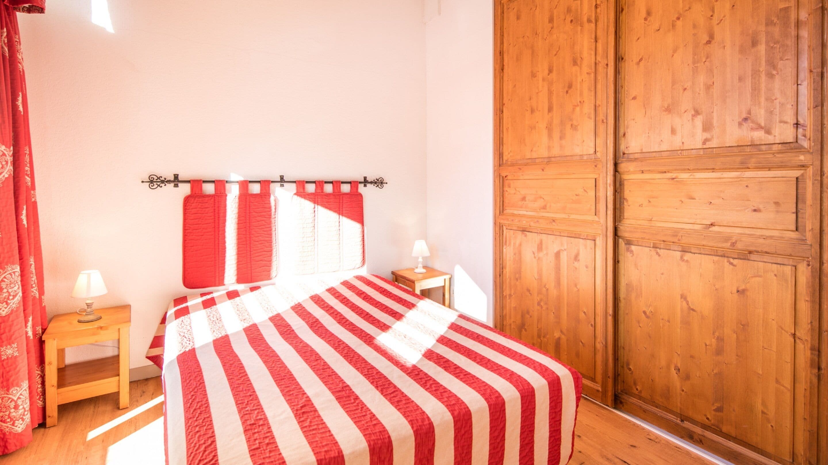 Ein Schlafzimmer mit einem Bett, zwei Nachttischen, einem Holzschrank und roten Vorhängen.
