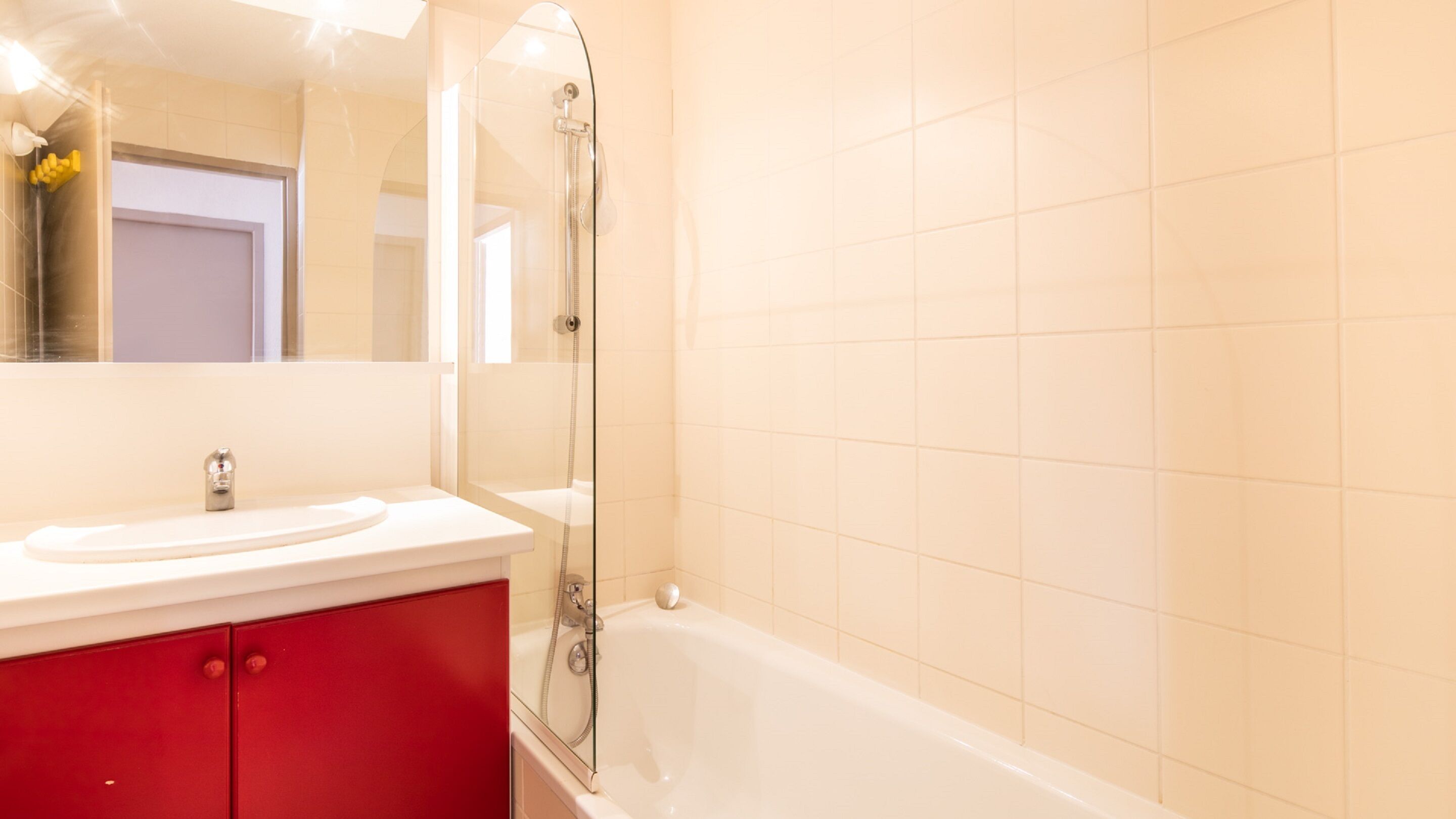 Un baño con una bañera blanca, ducha con mampara de vidrio y un mueble de almacenamiento rojo.