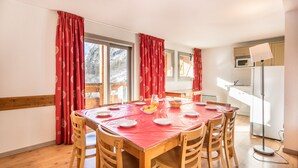 Comedor con mesa y sillas de madera, cortinas rojas y vista a un paisaje montañoso.