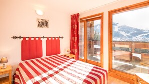 Un dormitorio con una cama grande, suelo de madera, ventana con vistas a la montaña y una cortina roja.