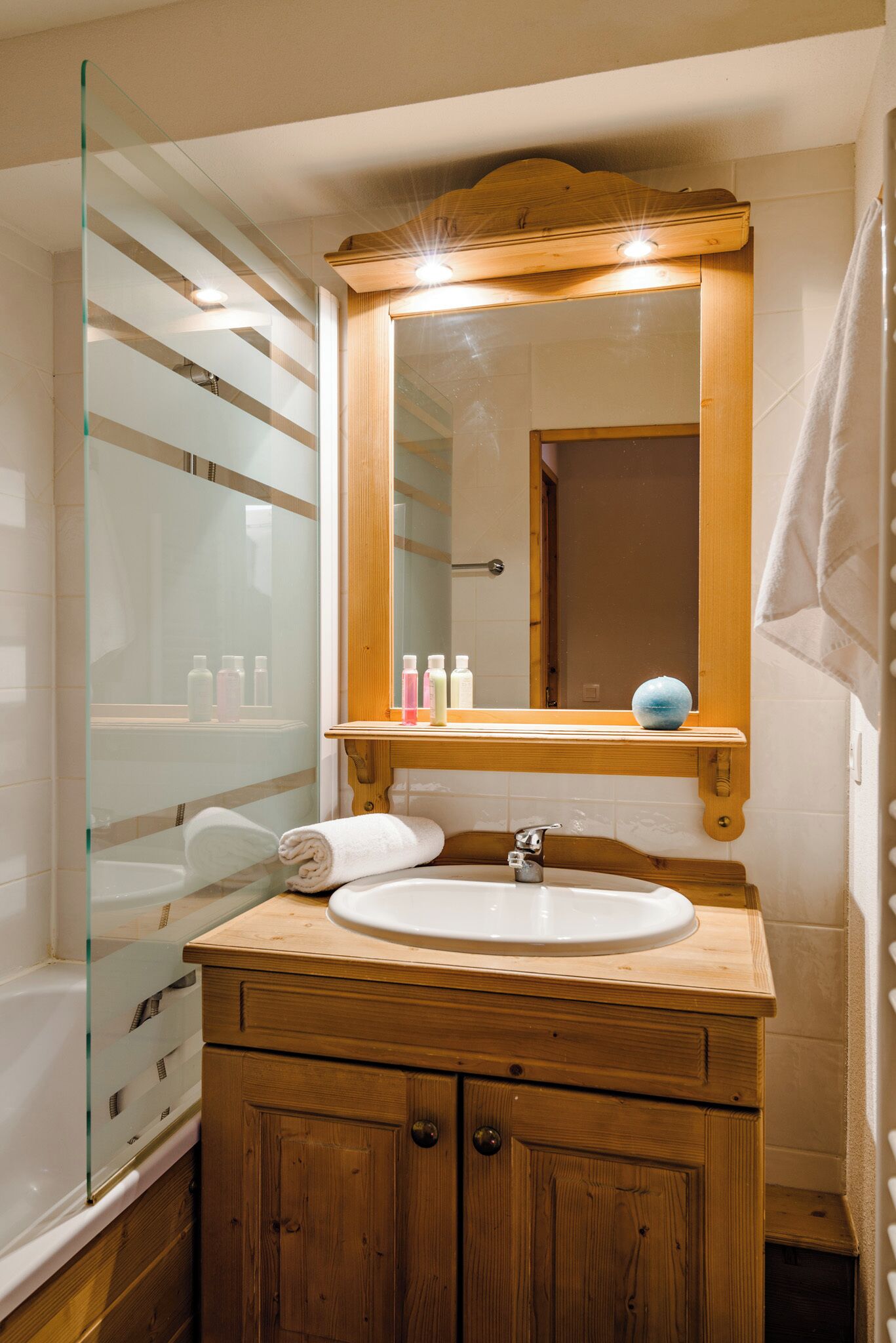 A bathroom with a wooden vanity, a glass shower enclosure, and a mirror above the sink.