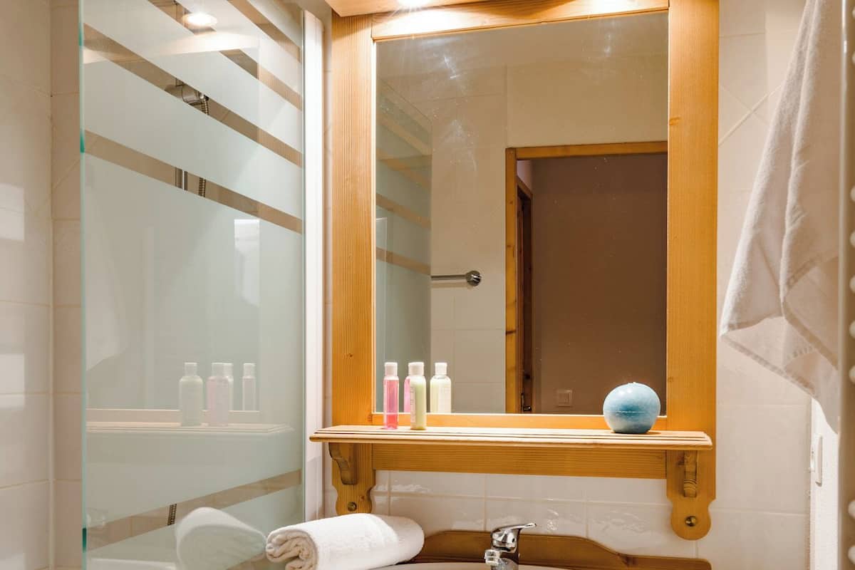 Ein Badezimmer mit einem Holzlaufschrank, einer Duschkabine aus Glas und einem Spiegel über dem Waschbecken.