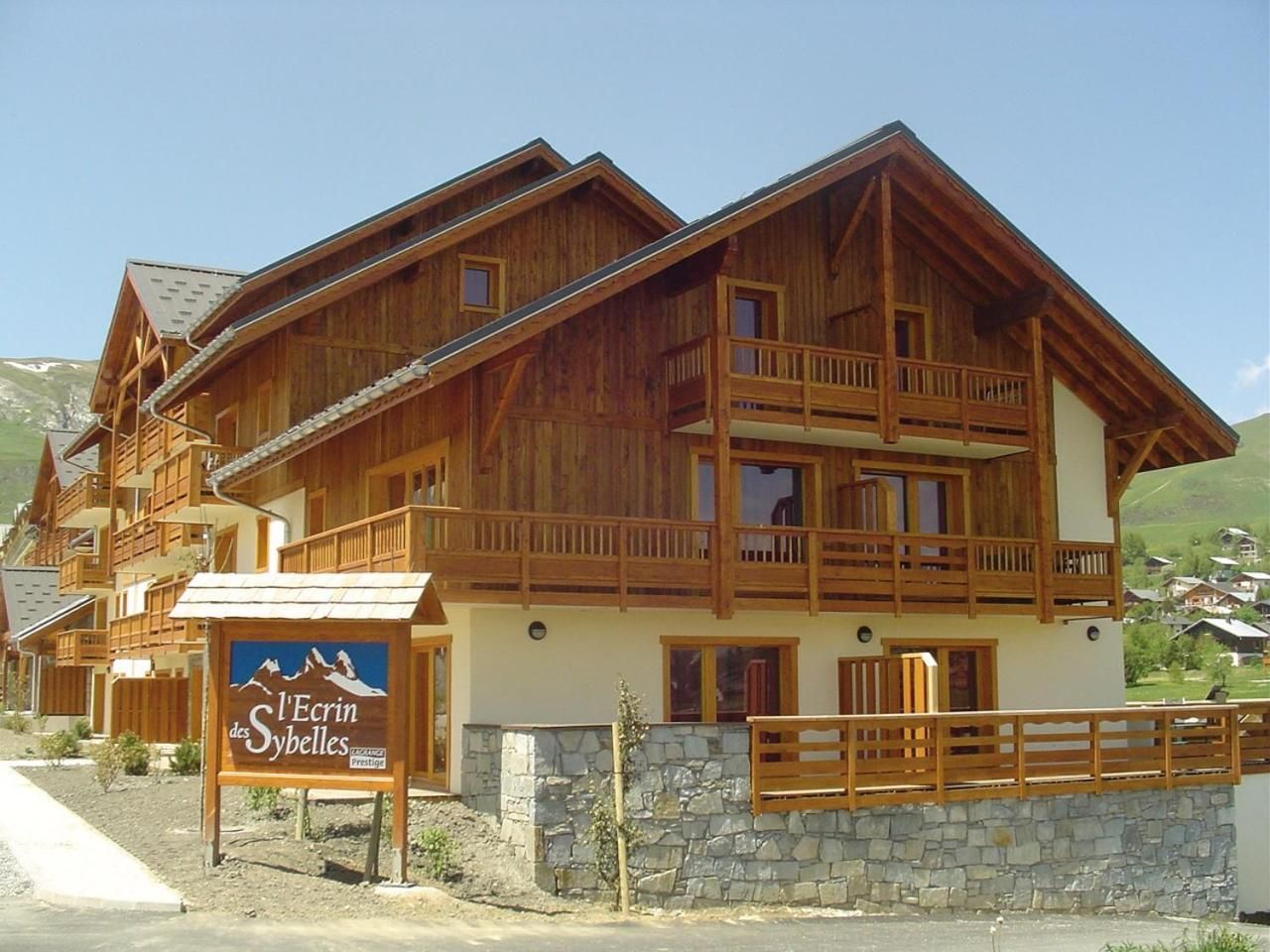 A wooden chalet with balconies, a stone foundation, and a sign indicating it's a mountain resort.