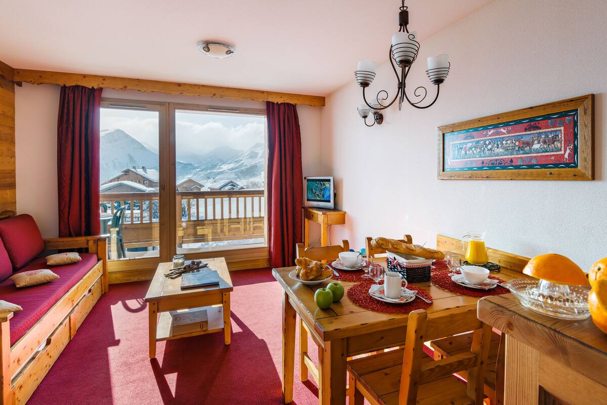 Ein gemütliches Zimmer mit einer Holzsofa, einem mit Frühstück gedeckten Esstisch, Blick auf Berge und einer Chandelier.