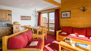 Una habitación acogedora con un sofá de madera, una mesa de comedor con sillas y una zona de cocina con armarios de madera.