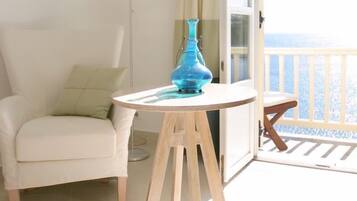 Un balcón con una silla blanca, una mesa redonda pequeña y un jarrón azul, además de una lámpara de pie.