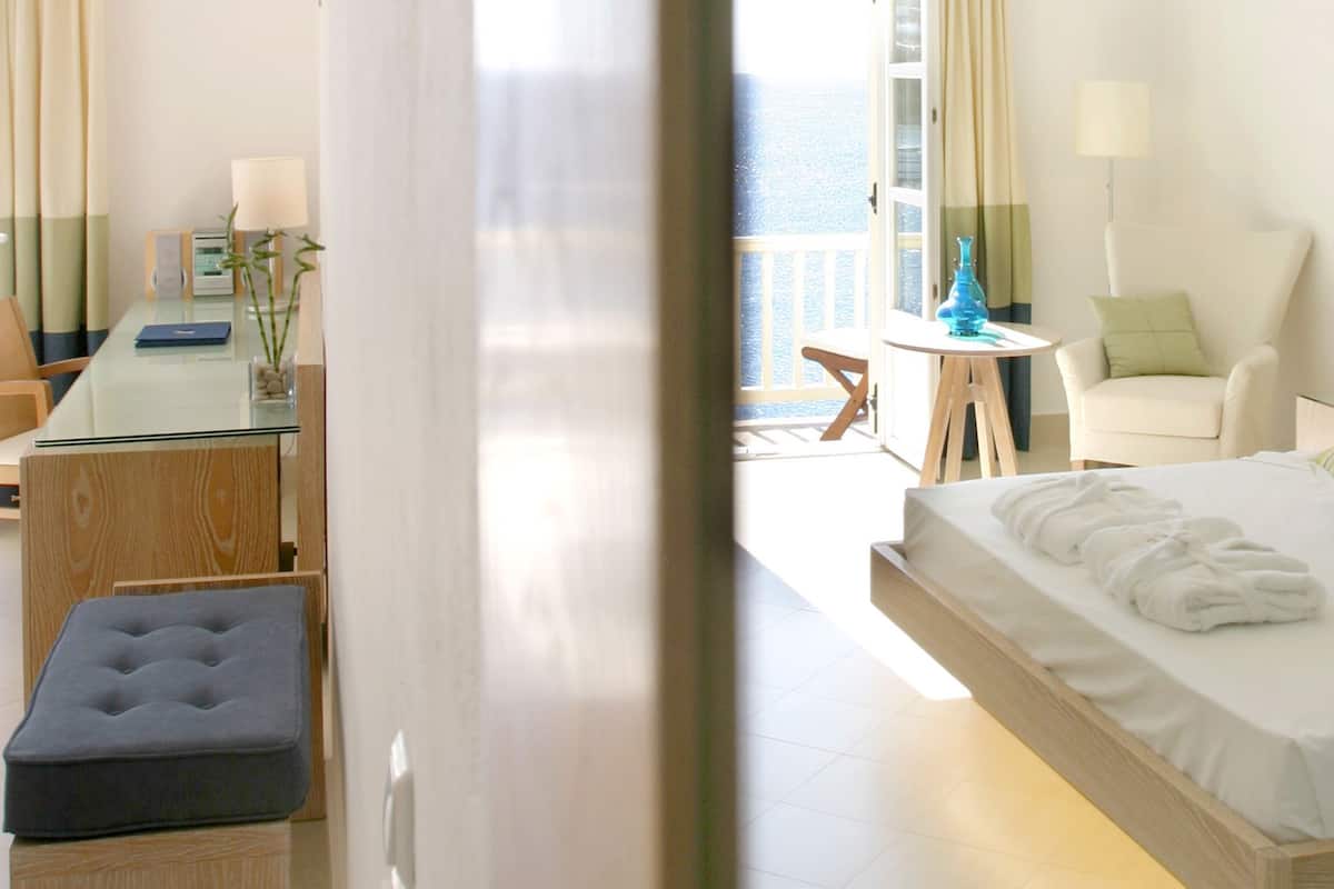 A hotel room with a bed, a desk, a chair, and a view of the sea.