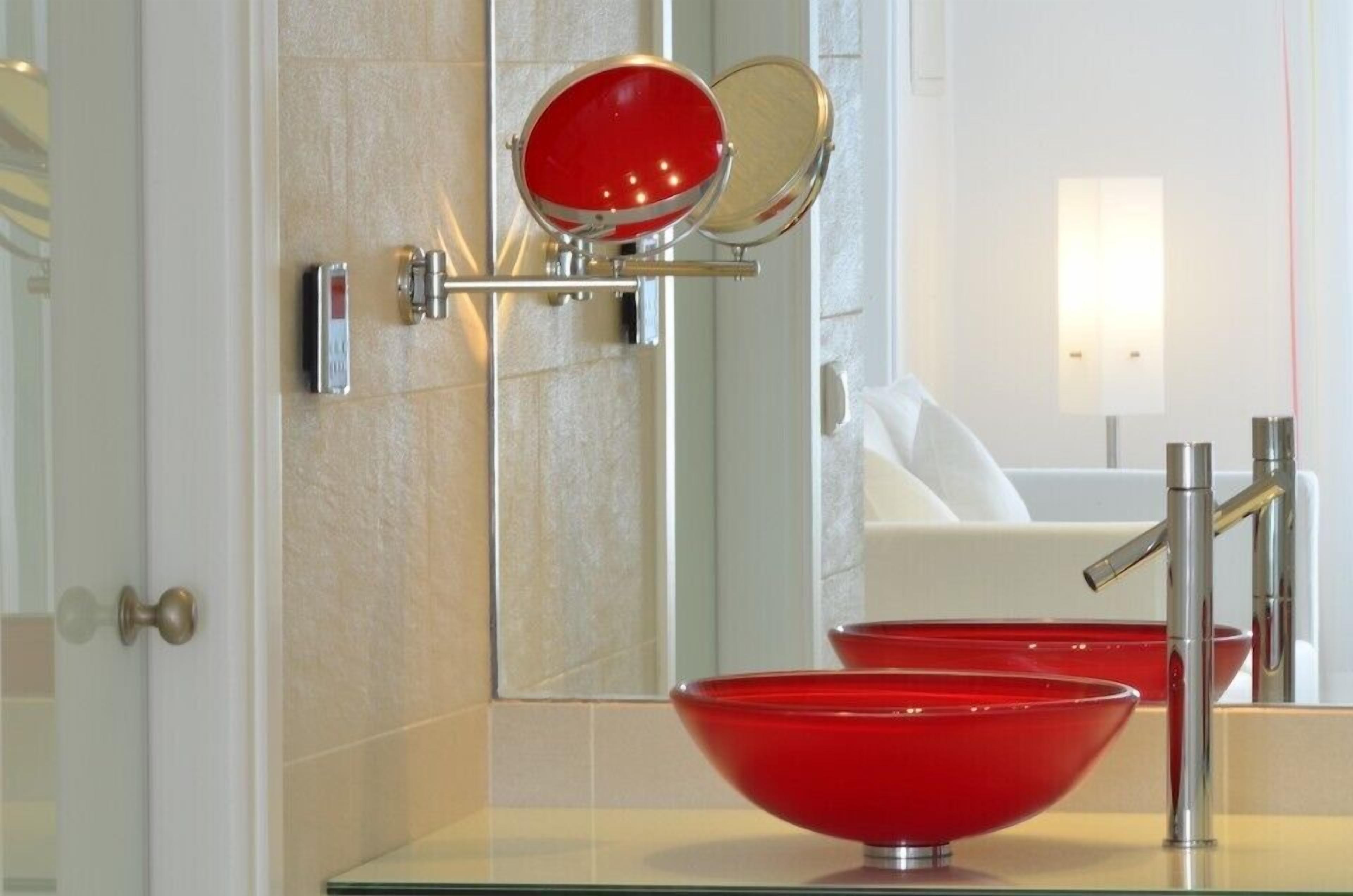 Une salle de bain moderne avec un lavabo en verre rouge, un miroir avec un cadre rouge et une baignoire blanche.