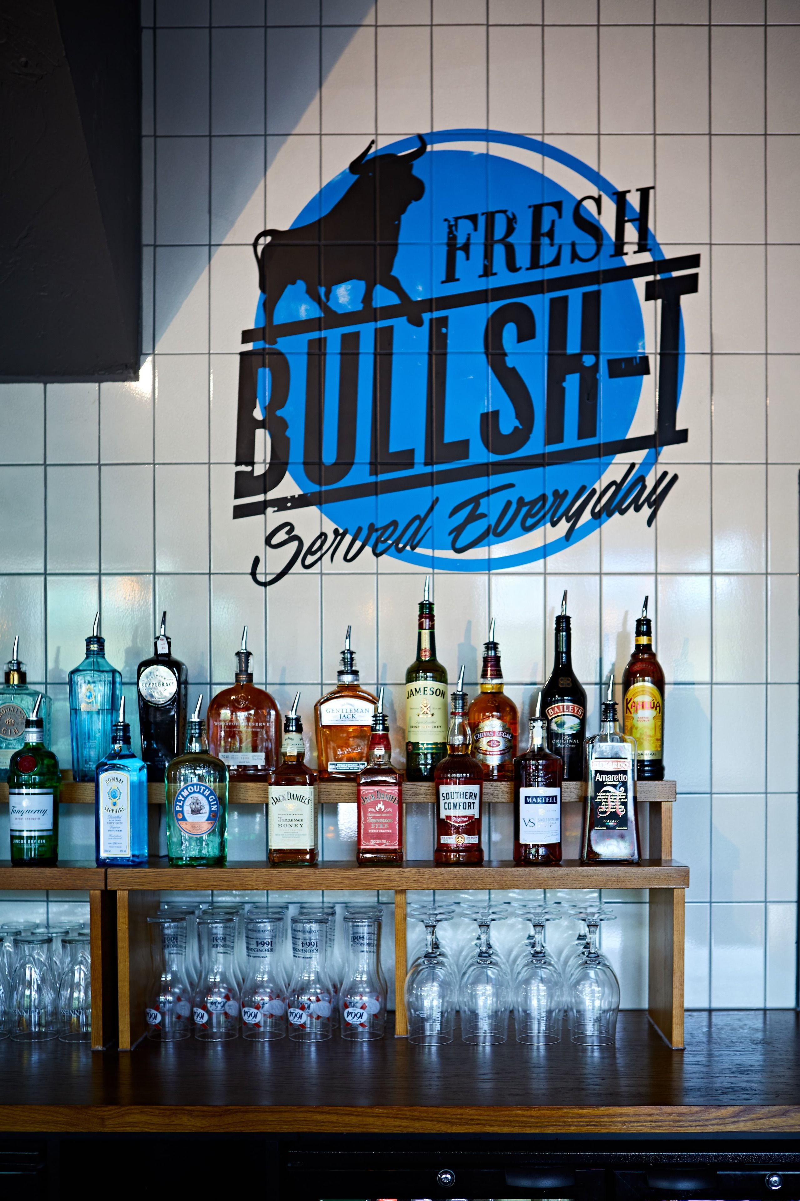 A bar area with a sign reading "FRESH BULLSH!" and various liquor bottles and glasses.