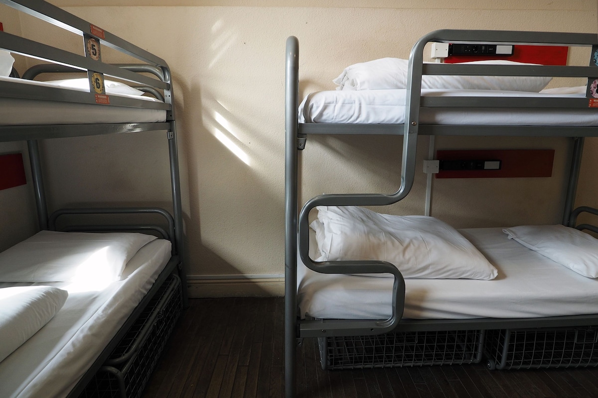 A bunk bed room with two beds, a wooden floor, and a wall with a light switch.