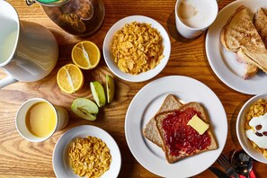A breakfast setting with cereal, toast, fruit, and beverages on a wooden table. - St Christopher's Inn, Greenwich - Hostel (London)