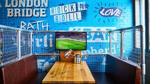 A sports bar with a large TV screen, a menu board, and a blue brick wall with "LONDON BRIDGE ROCK N ROLL" and "LOVE" written on it. - St Christopher's Inn, Greenwich - Hostel (London)