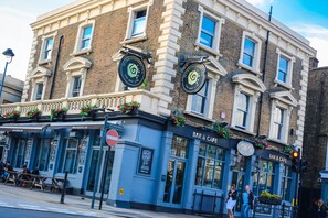 A building with a bar and cafe on the ground floor, featuring large windows and a sign with a logo. - St Christopher's Inn, Greenwich - Hostel (London)