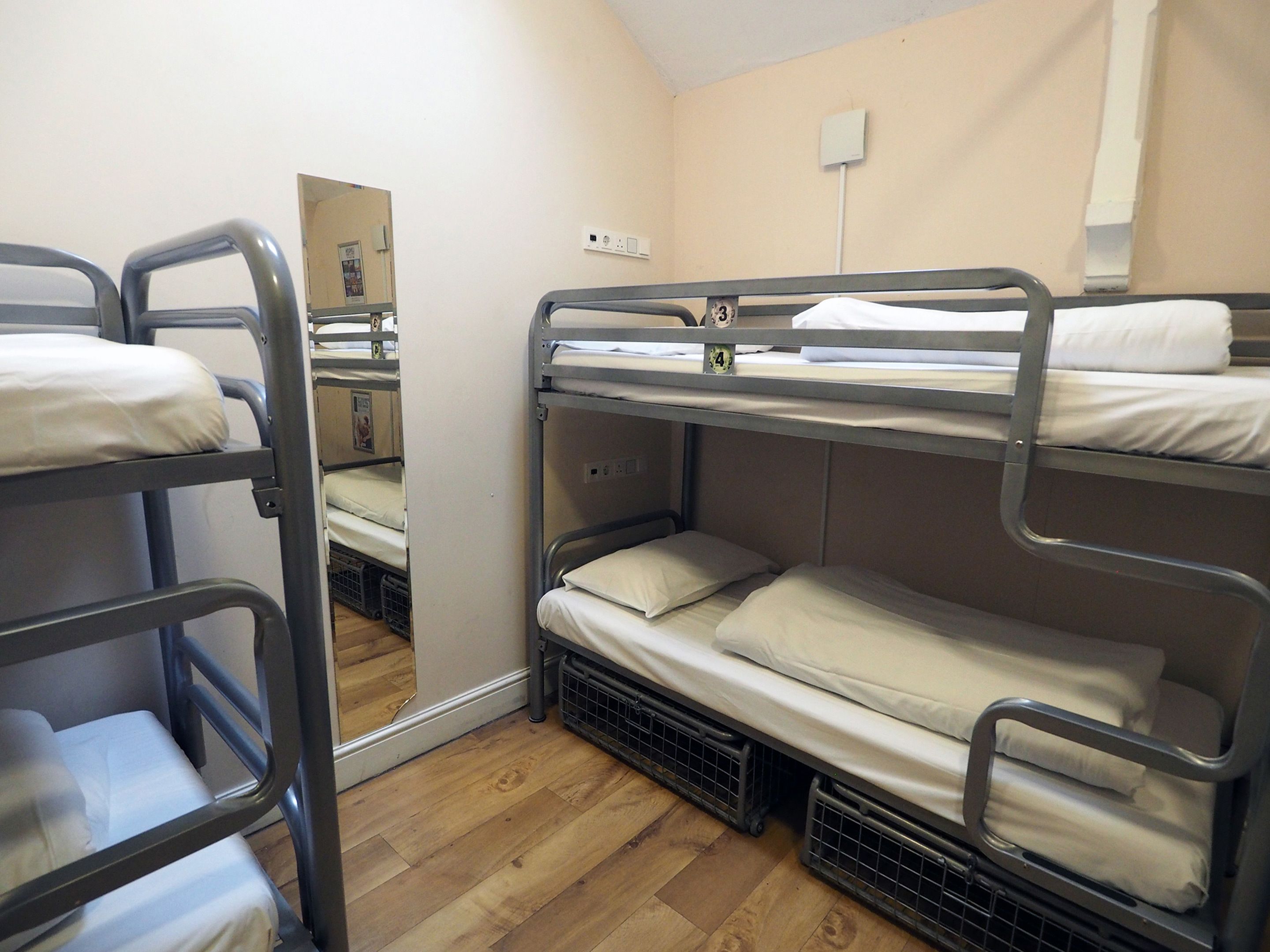 Une chambre avec des lits superposés, un plancher en bois, un miroir et une prise électrique au mur.