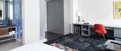 Une chambre d’hôtel moderne équipée d’un lit, d’un bureau avec une chaise, d’une armoire et d’une salle de bain avec douche.